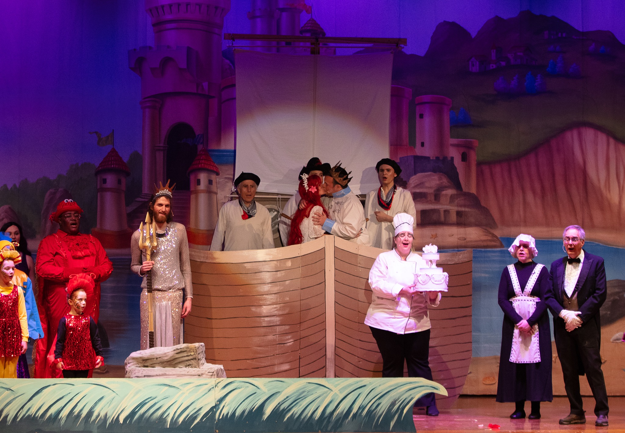 Ariel and Eric on a boat surrounded by other characters from the play